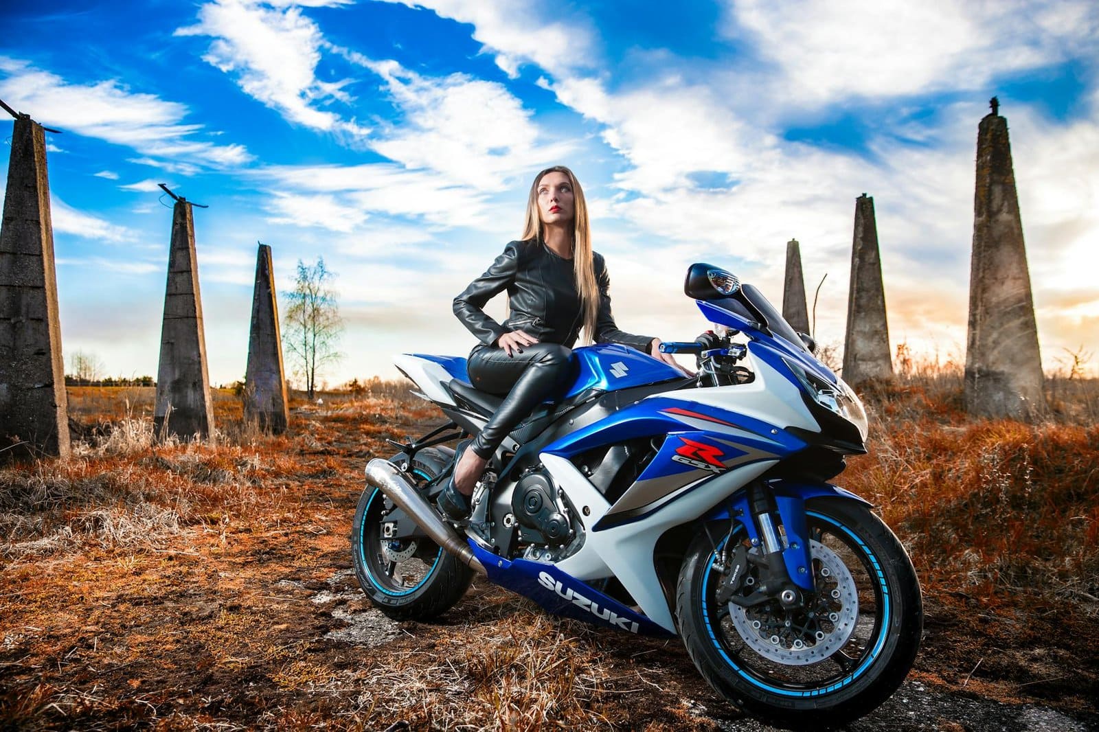woman in black leather jacket sitting on blue and white suzuki gsx r
